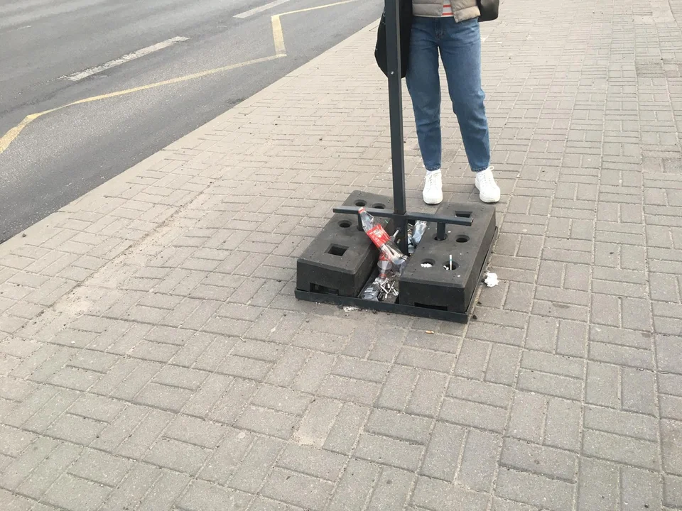 Podróżni MPK Łódź oczekują na autobus na przystanku bez wiaty, ławki i śmietnika.